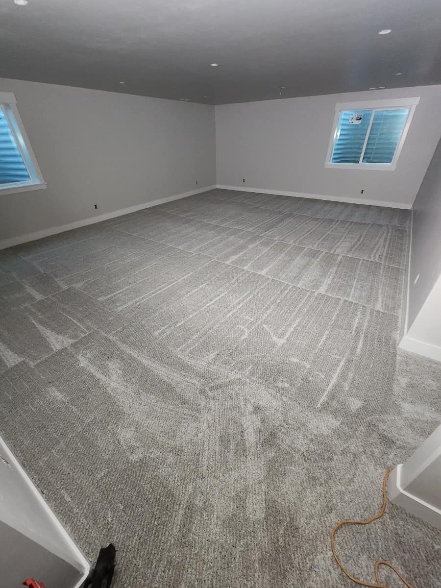 An empty room with a large carpeted floor and two windows.