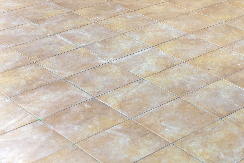 Diamond-patterned beige tile flooring with subtle color variations and textured appearance.