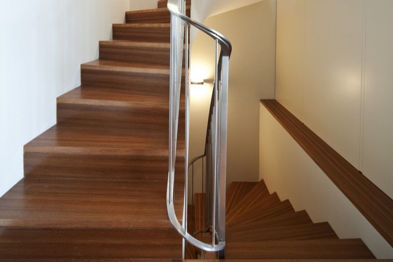 Wooden curved staircase with metal railing in a well-lit interior.