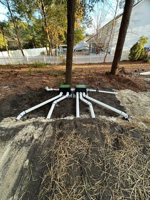 A drainage system is being installed in the dirt in the backyard of a house.