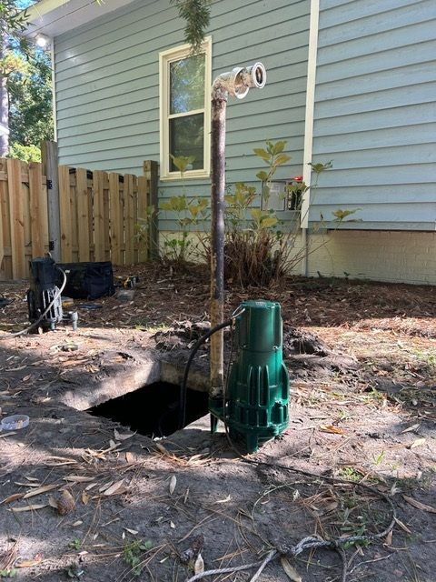 A green pump is sitting in the dirt in front of a house.