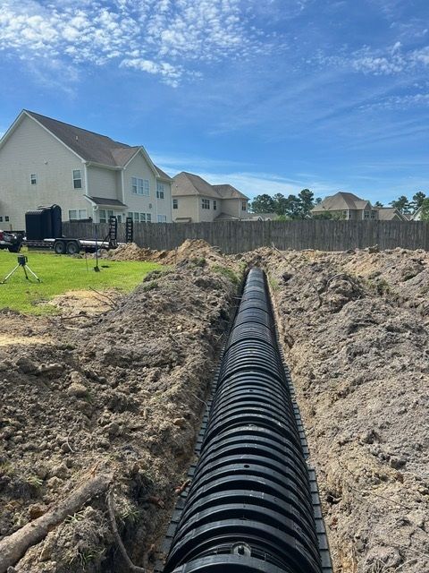 A large black pipe is laying in the dirt in front of a house.