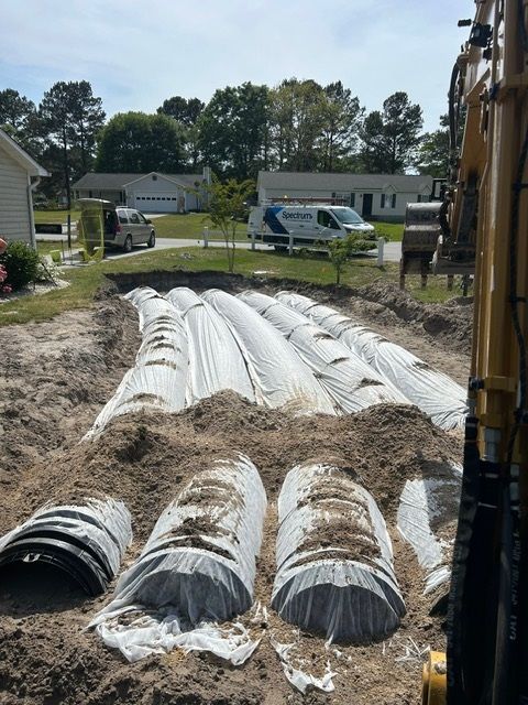 A bunch of pipes are sitting in the dirt in front of a house