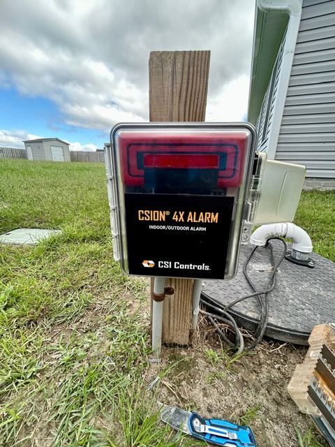 A csion 4x alarm is sitting on a wooden post in the grass.