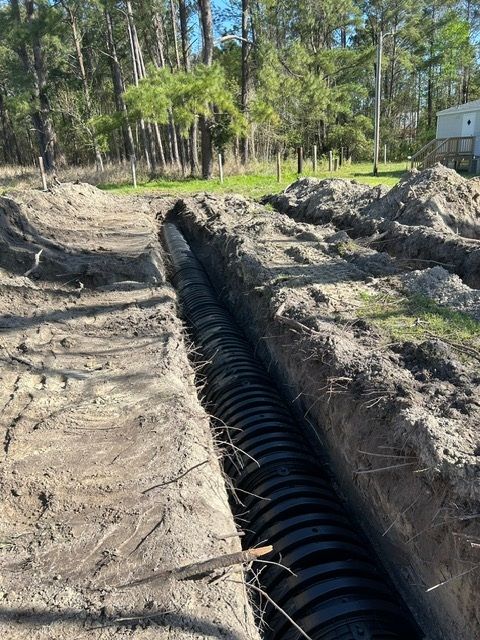 A large black pipe is being installed in the dirt.
