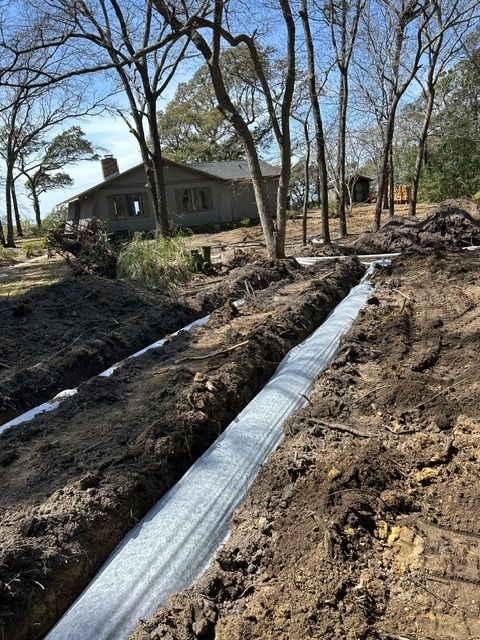 A drainage system is being installed in the dirt in front of a house.