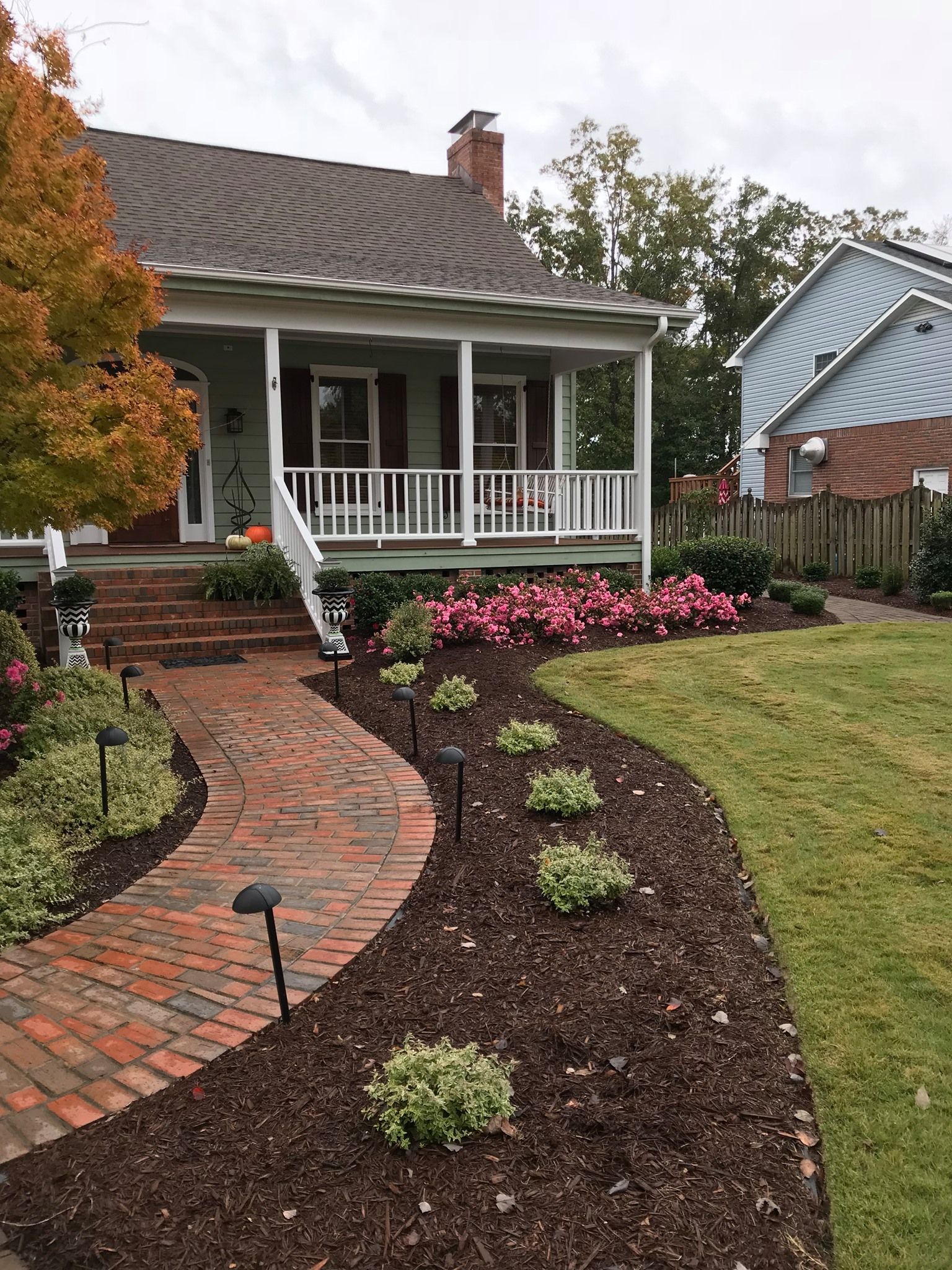 A house with a porch and a brick walkway leading to it.