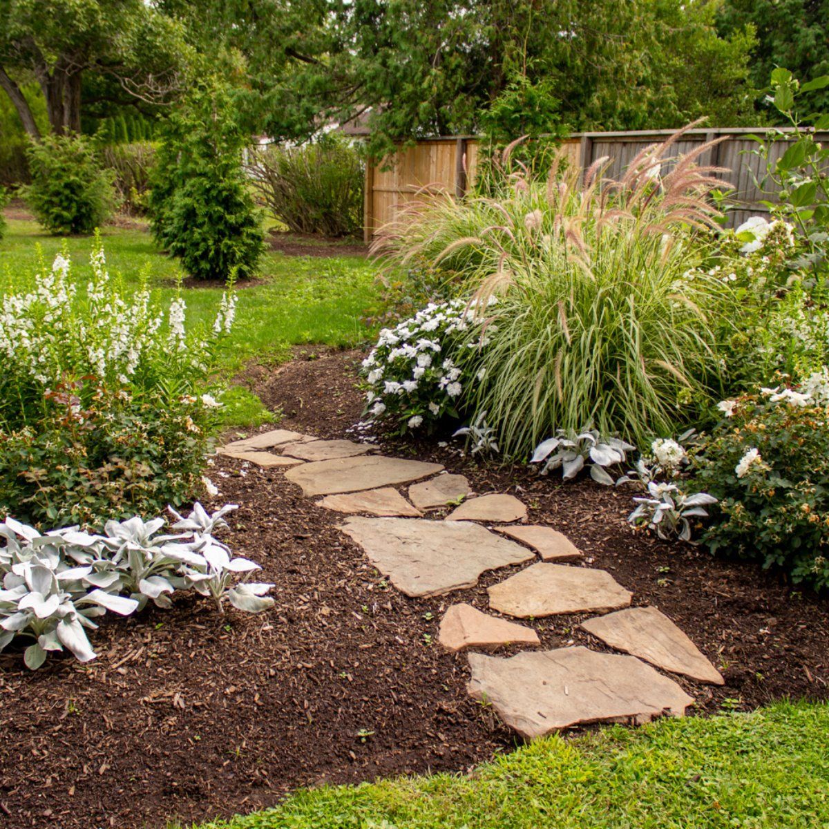 A stone walkway in a garden surrounded by flowers and shrubs.