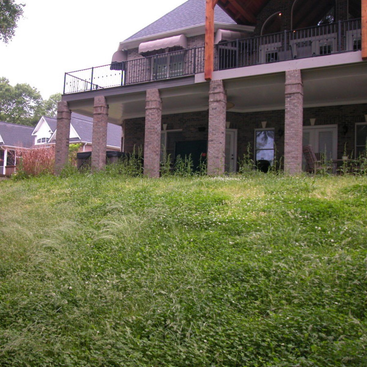 A large house with a balcony sits on top of a grassy hill