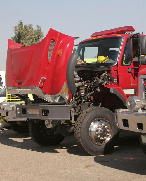 Red fire truck with a smashed front hood and damaged bumper on a roadside