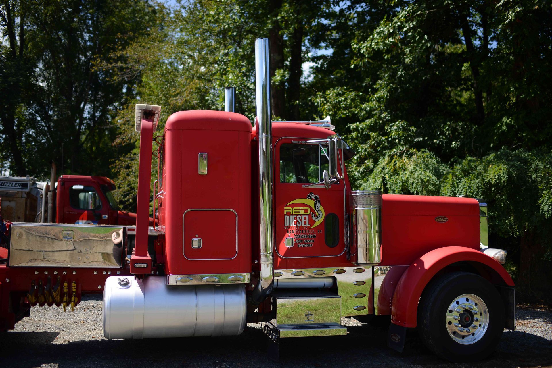 Red semi-truck parked outdoors beside trees and a wooden flatbed trailer.