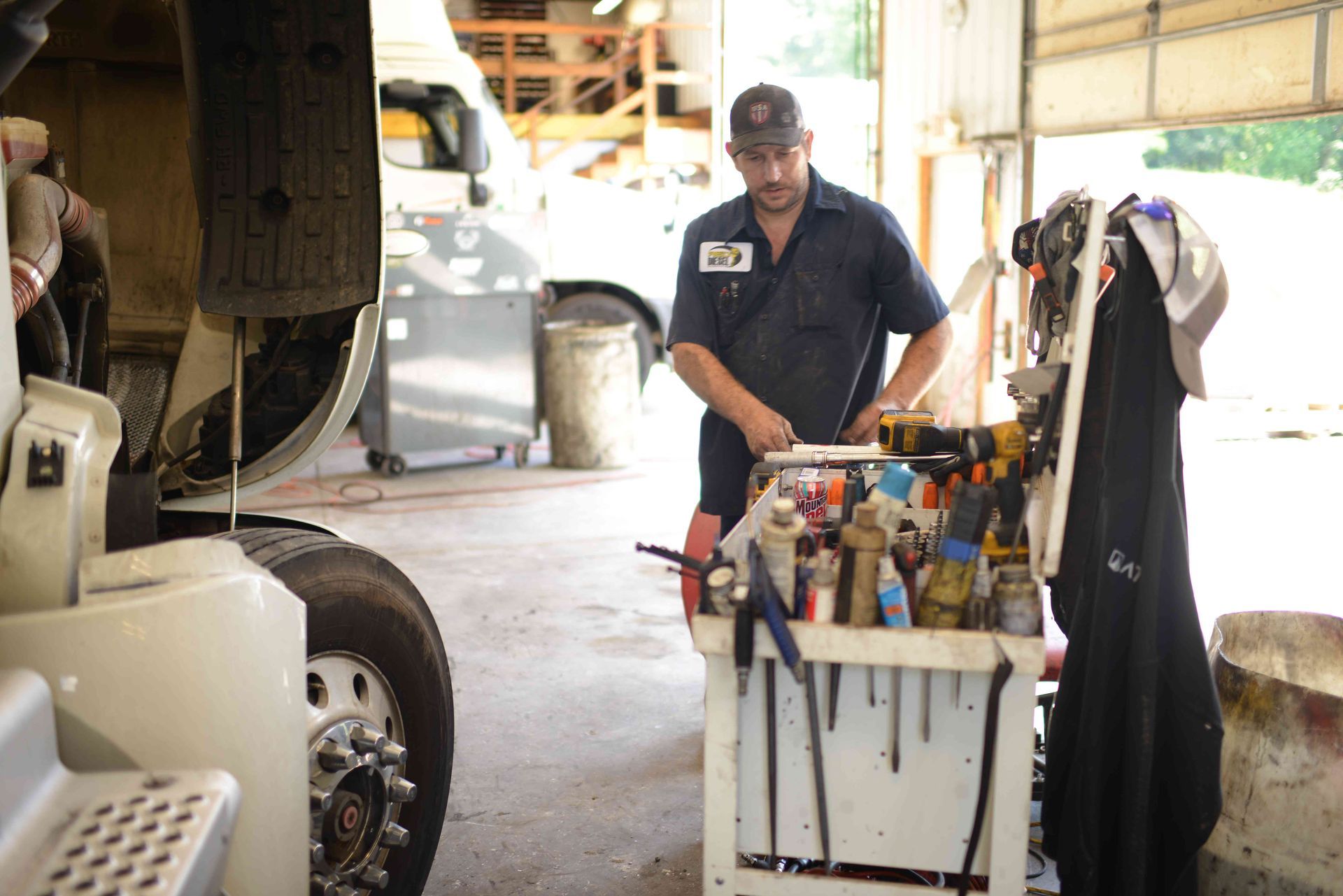 Mechanic standing by a tool cart in an auto repair garage, with a car and shop equipment nearby.