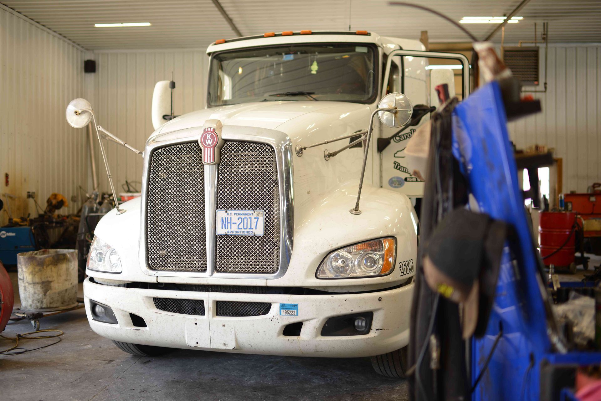 White semi-truck in a garage, with a person working beside it and tools in the background.