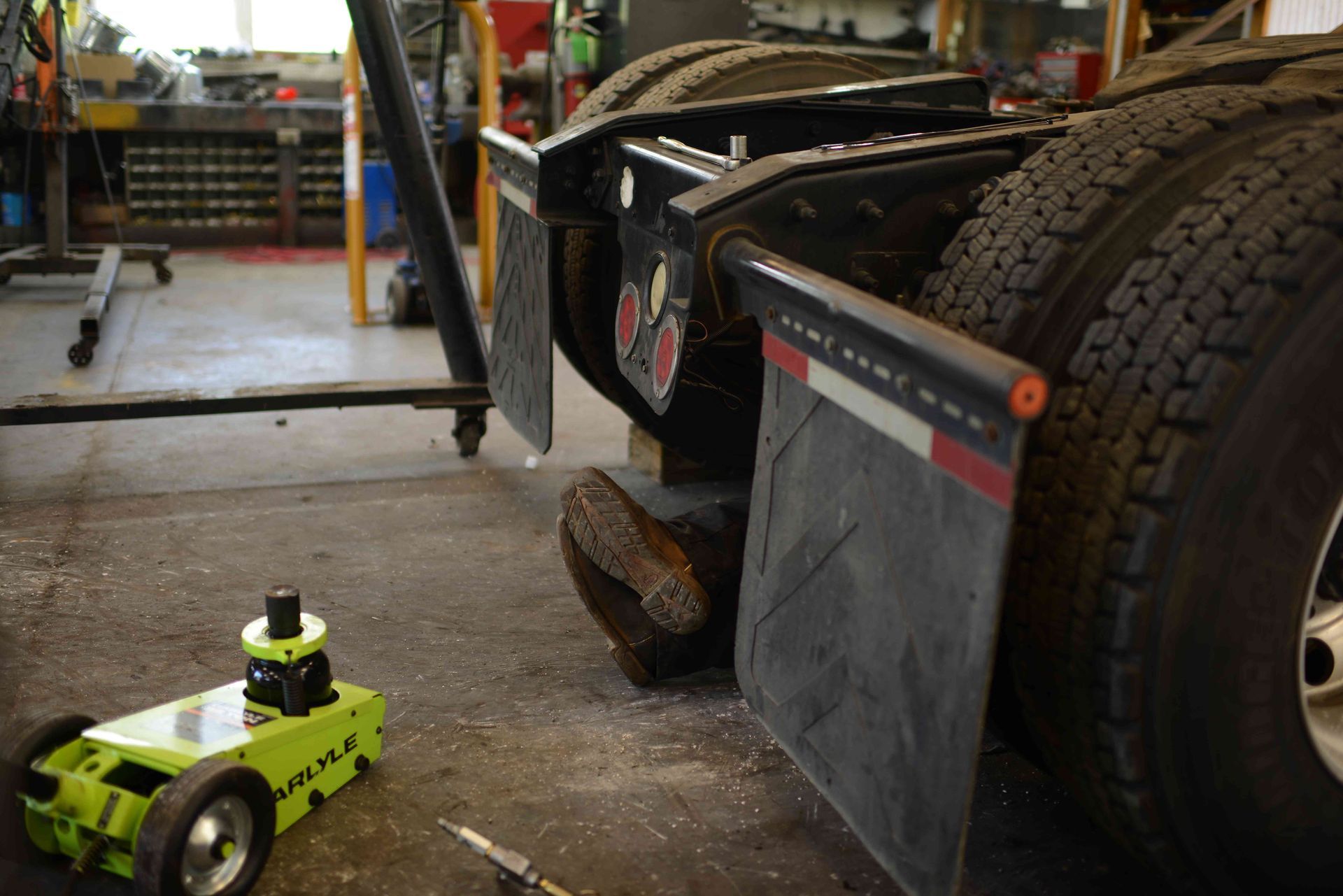 Green remote-control car beside a large truck tire in a garage workshop