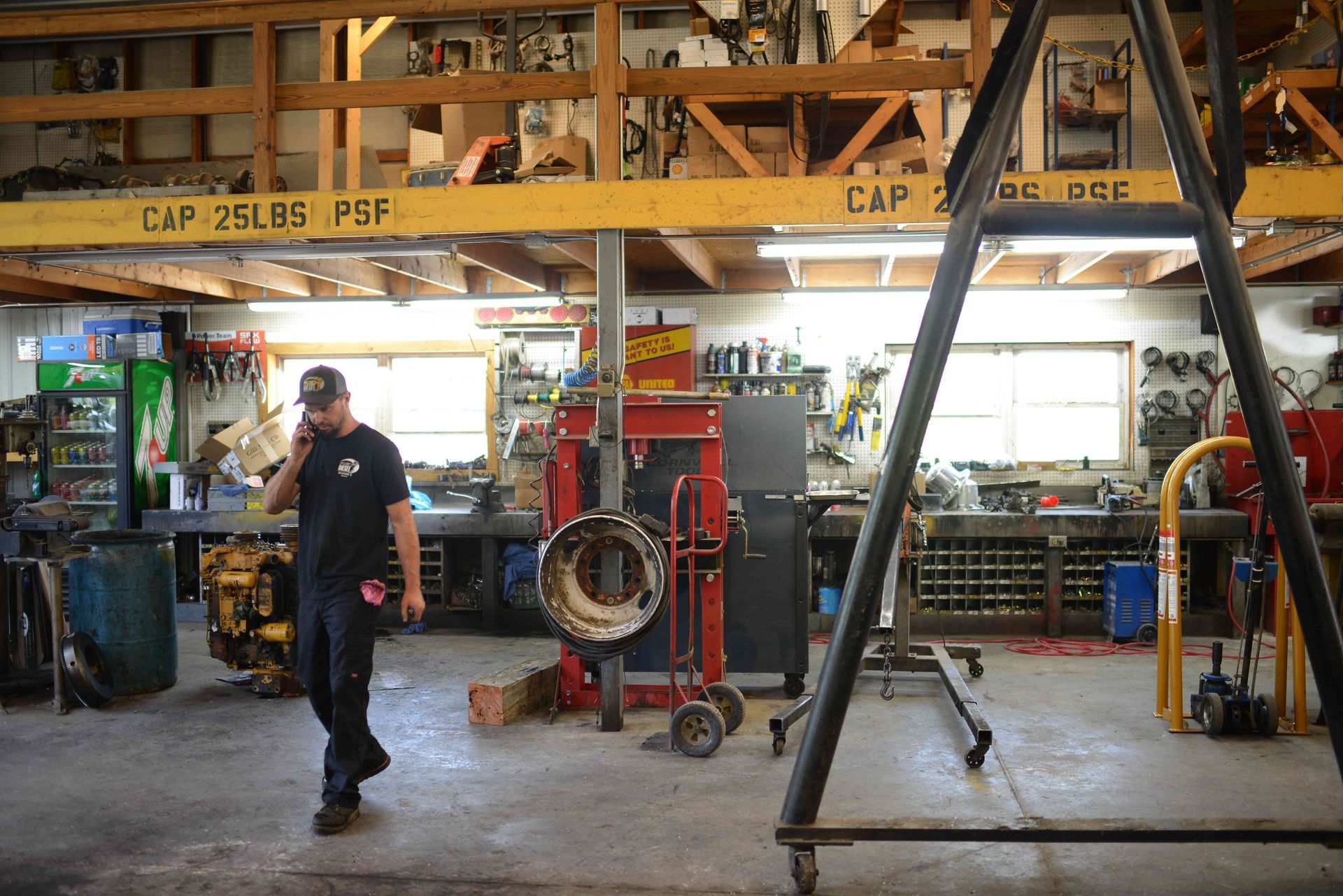 Worker in a cluttered workshop beside machinery and a large hanging tire
