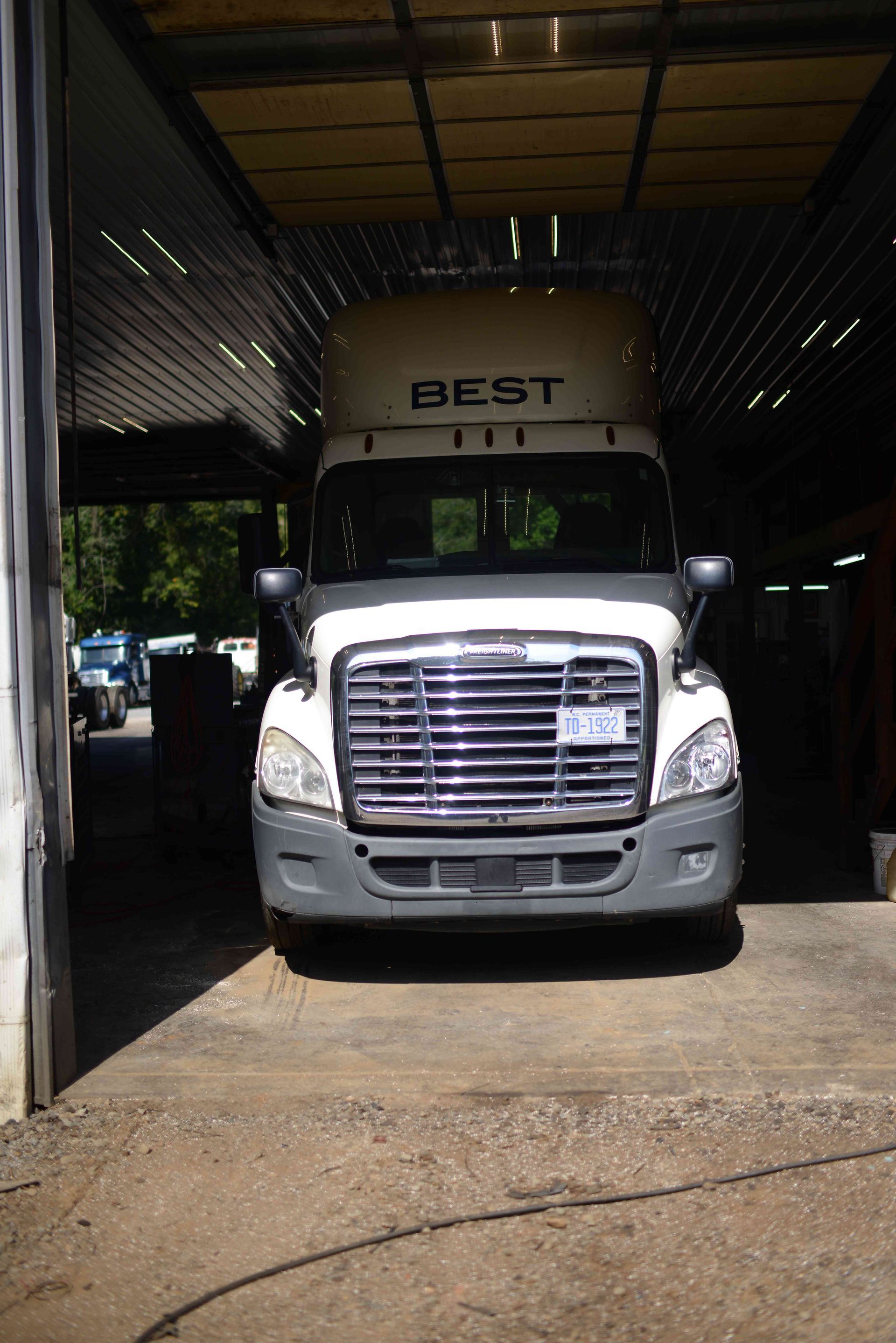 White freight truck parked in a garage doorway, front view with “BEST” on the cab.