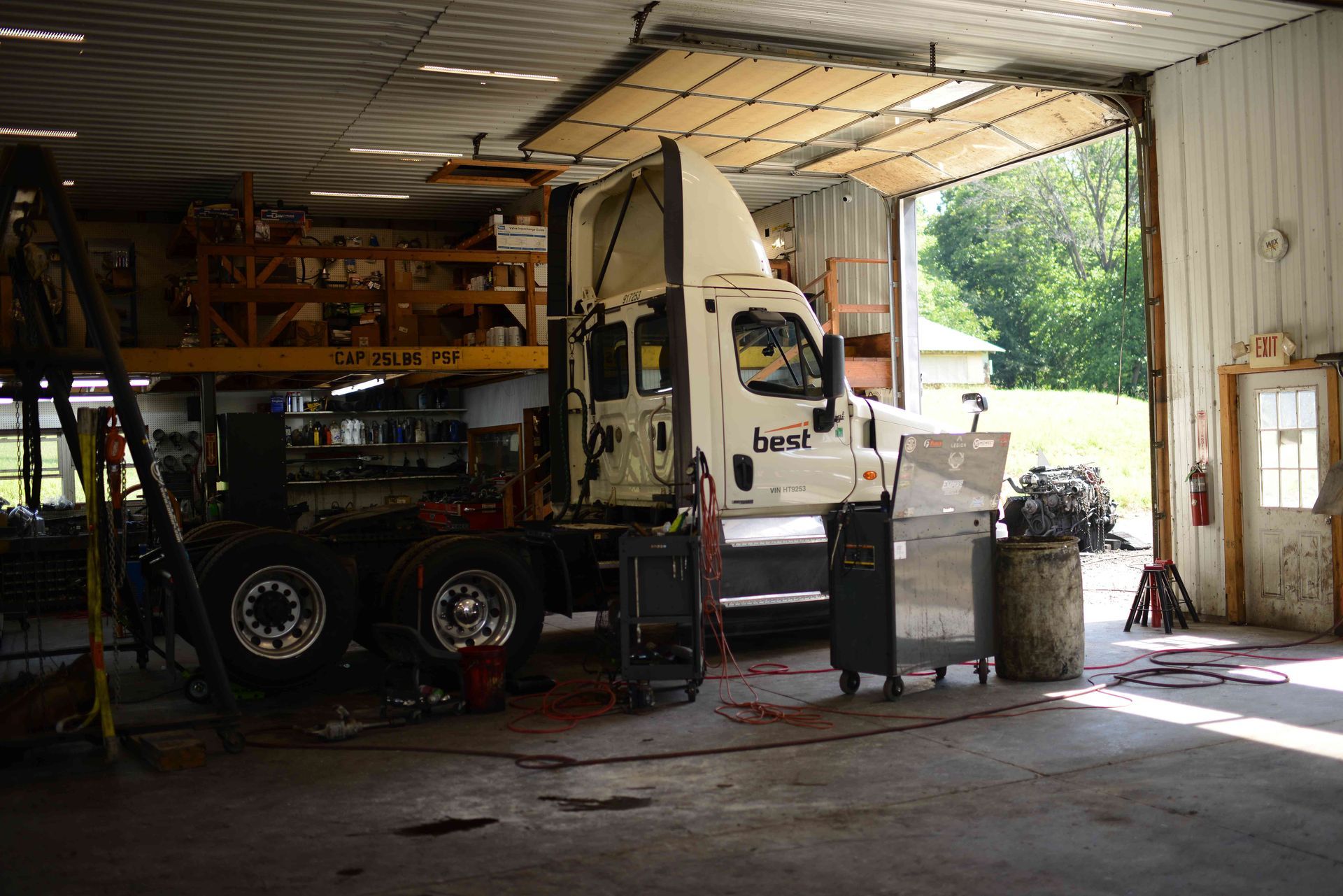 Truck parked inside a cluttered garage with equipment and an open door letting in daylight