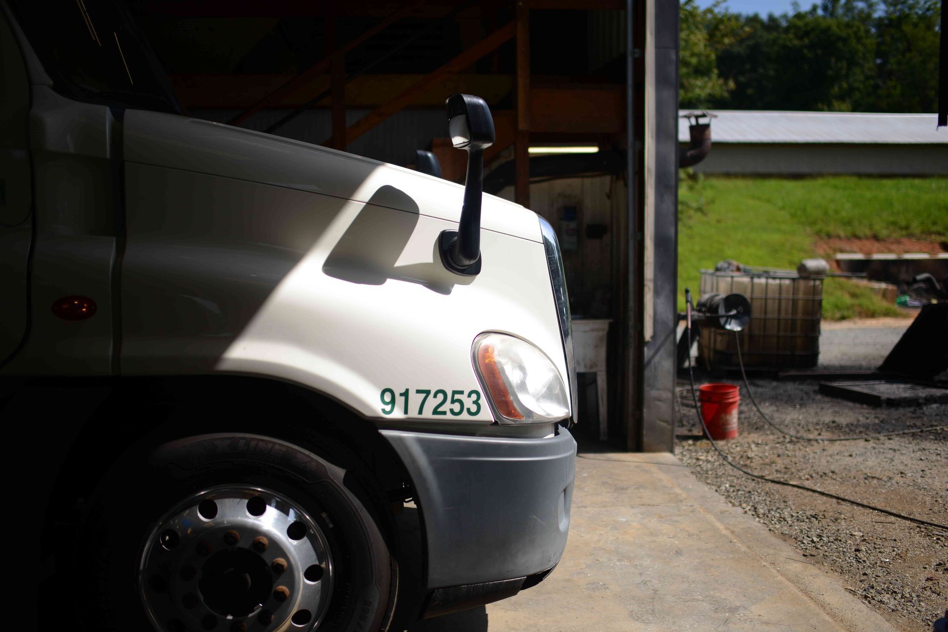 White semi truck parked at a garage bay beside a red fuel can and grassy yard