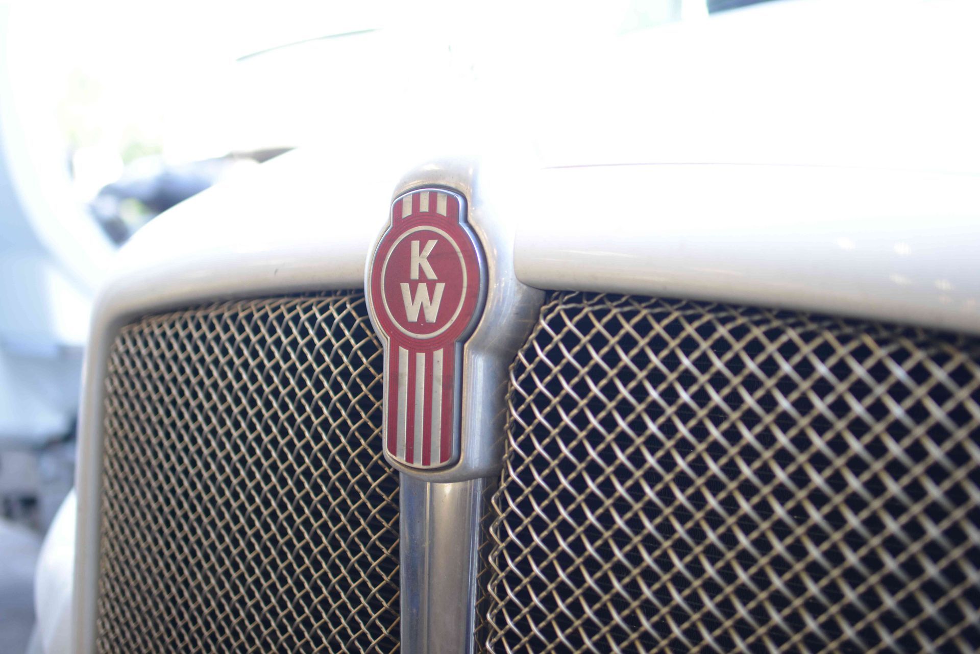 Close-up of a white Kenworth truck grille with the red KW emblem.