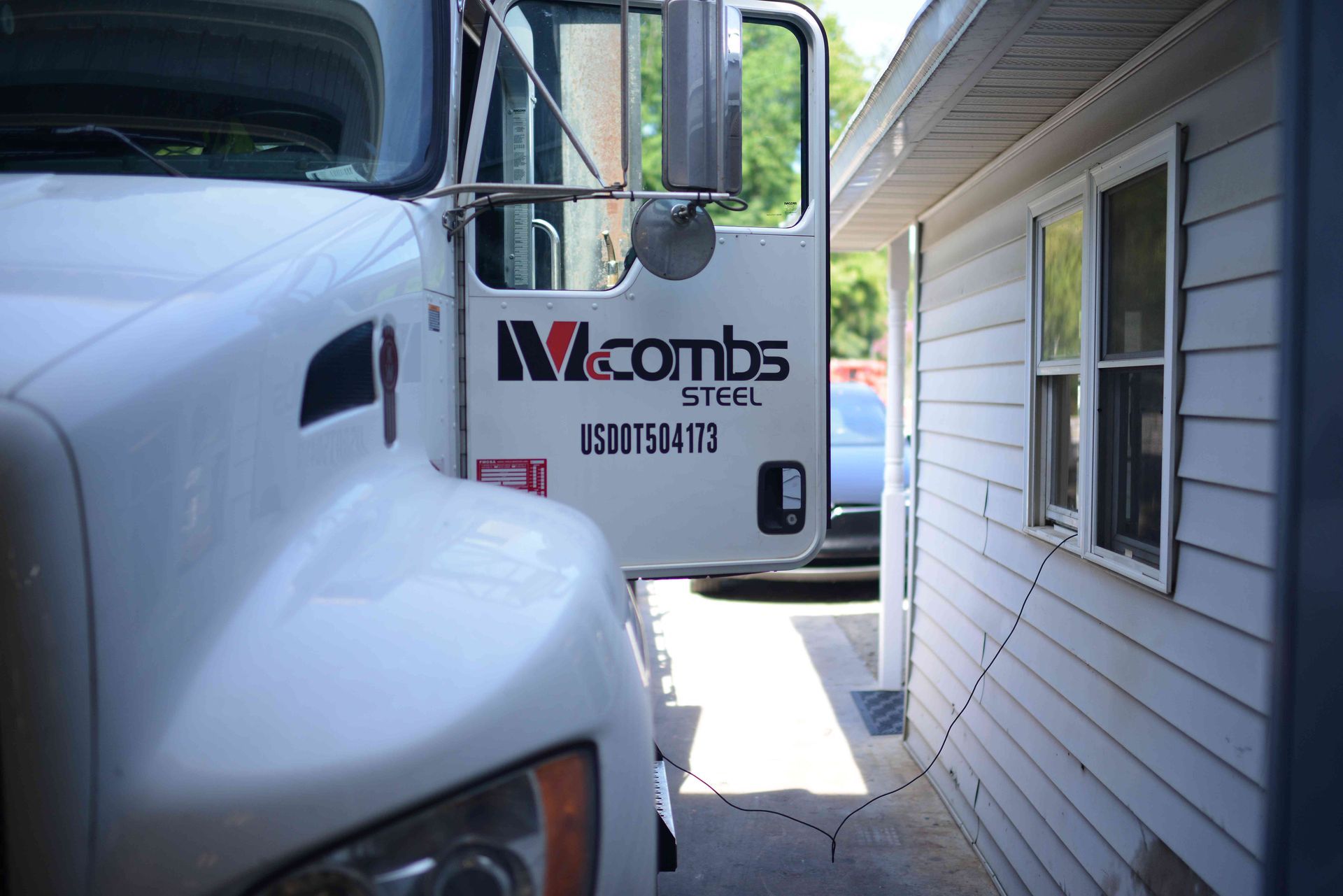 White work truck parked beside a house, with the driver door open and a company logo visible.