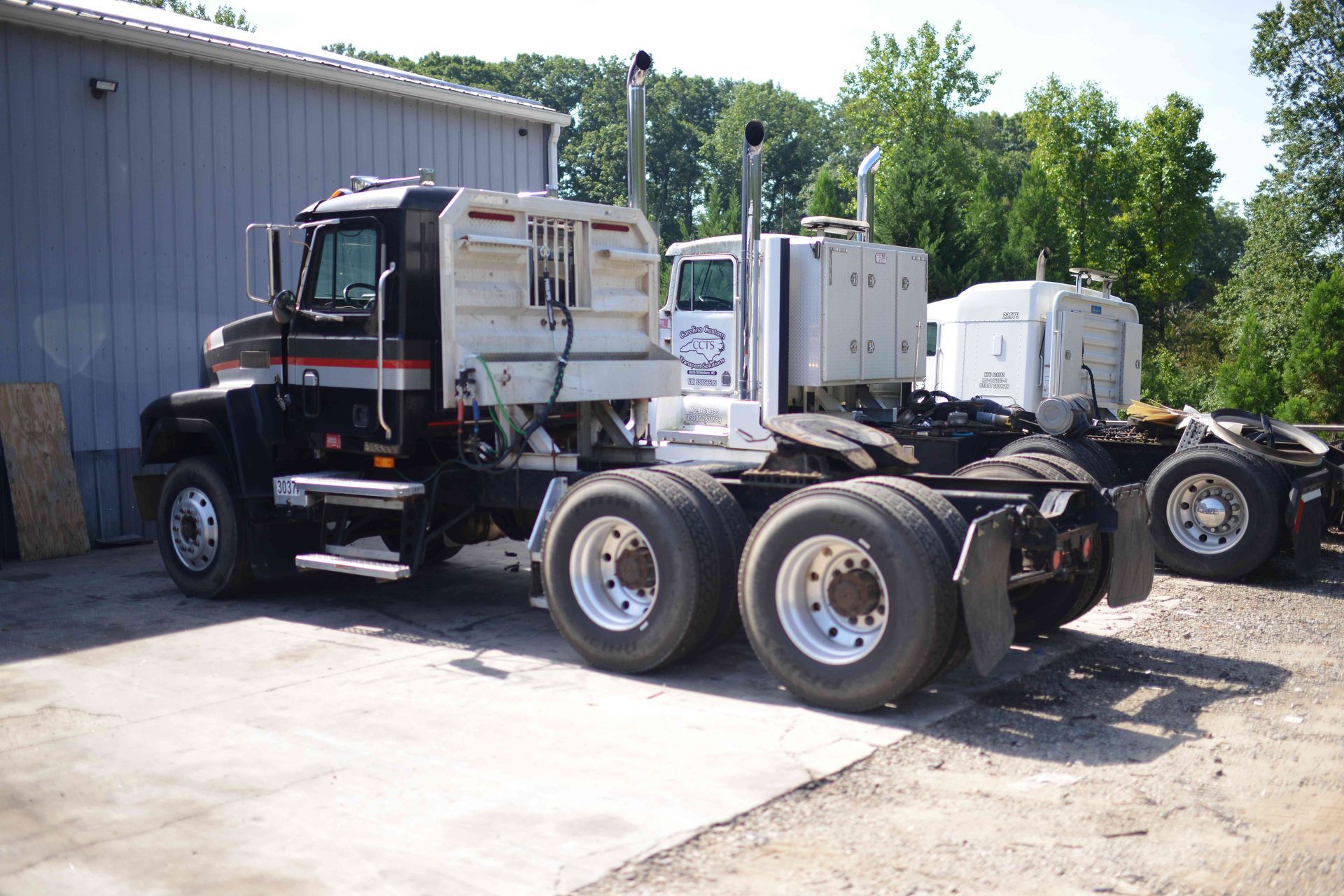 Black semi-truck chassis parked beside a gray building in a sunny industrial lot