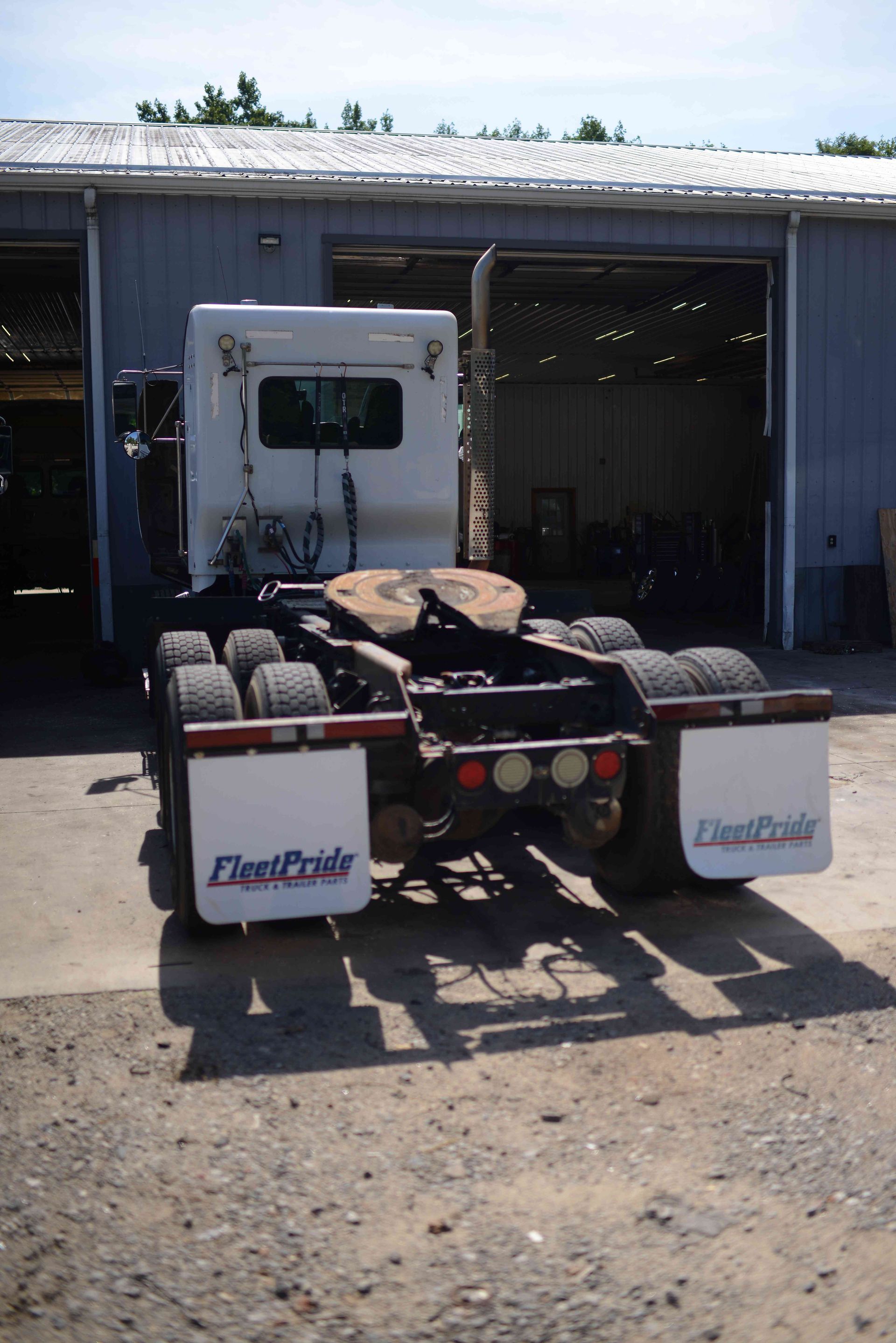 Truck chassis parked in front of a metal garage, with rear dual wheels and white fenders