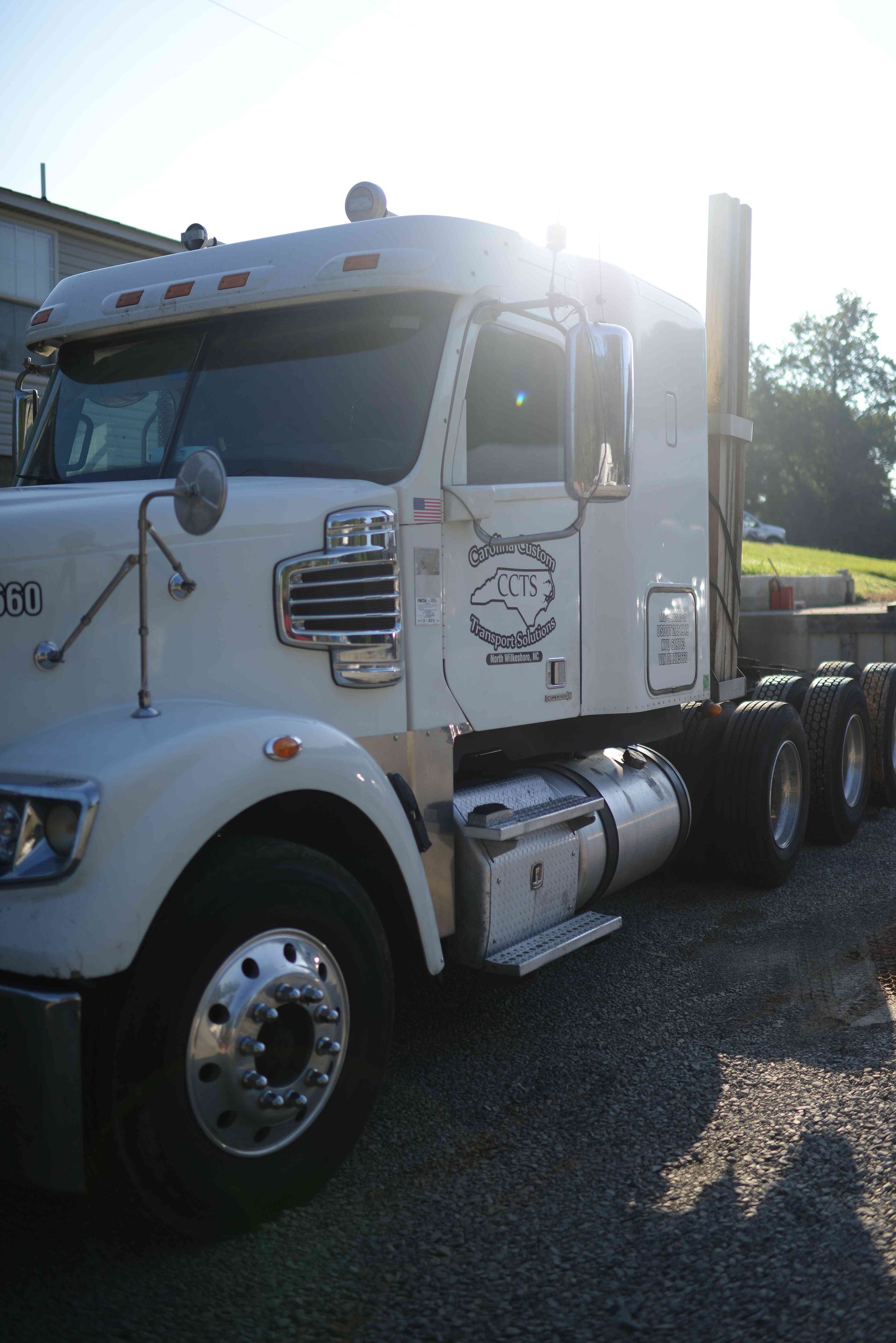 White semi-truck cab parked in sunlight on a gravel lot