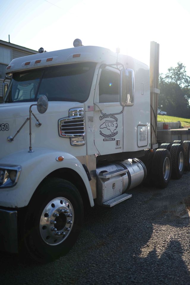 White semi-truck parked on gravel in bright sunlight, side view with chrome details and trailer hitch