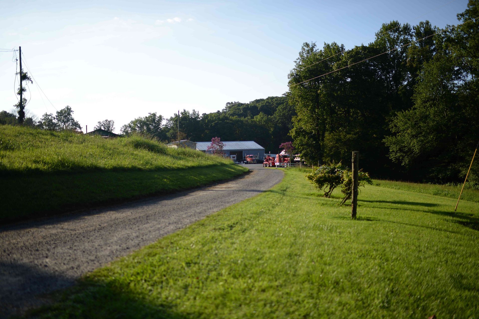Curving gravel path through a green park toward distant farm buildings under a clear sky