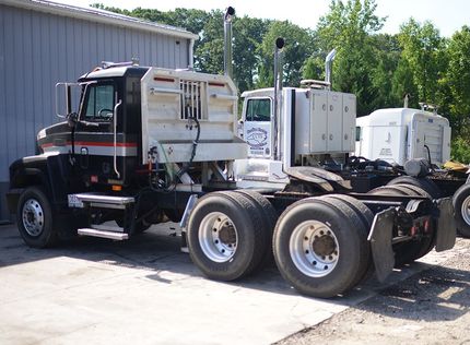 Black semi truck cab and chassis parked beside a building, viewed from the side.