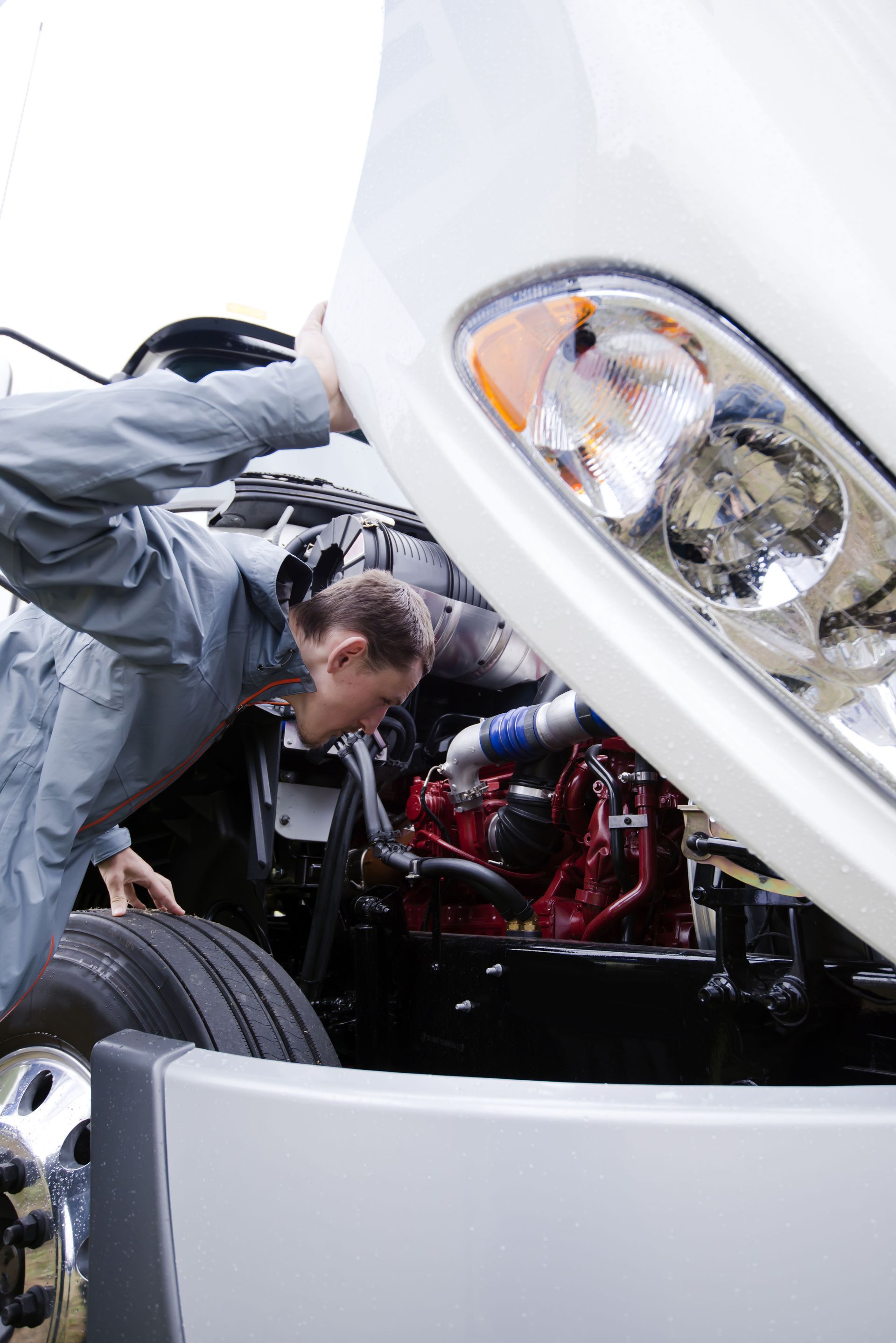 Mechanic inspecting engine under raised white car hood, with tools and front tire visible