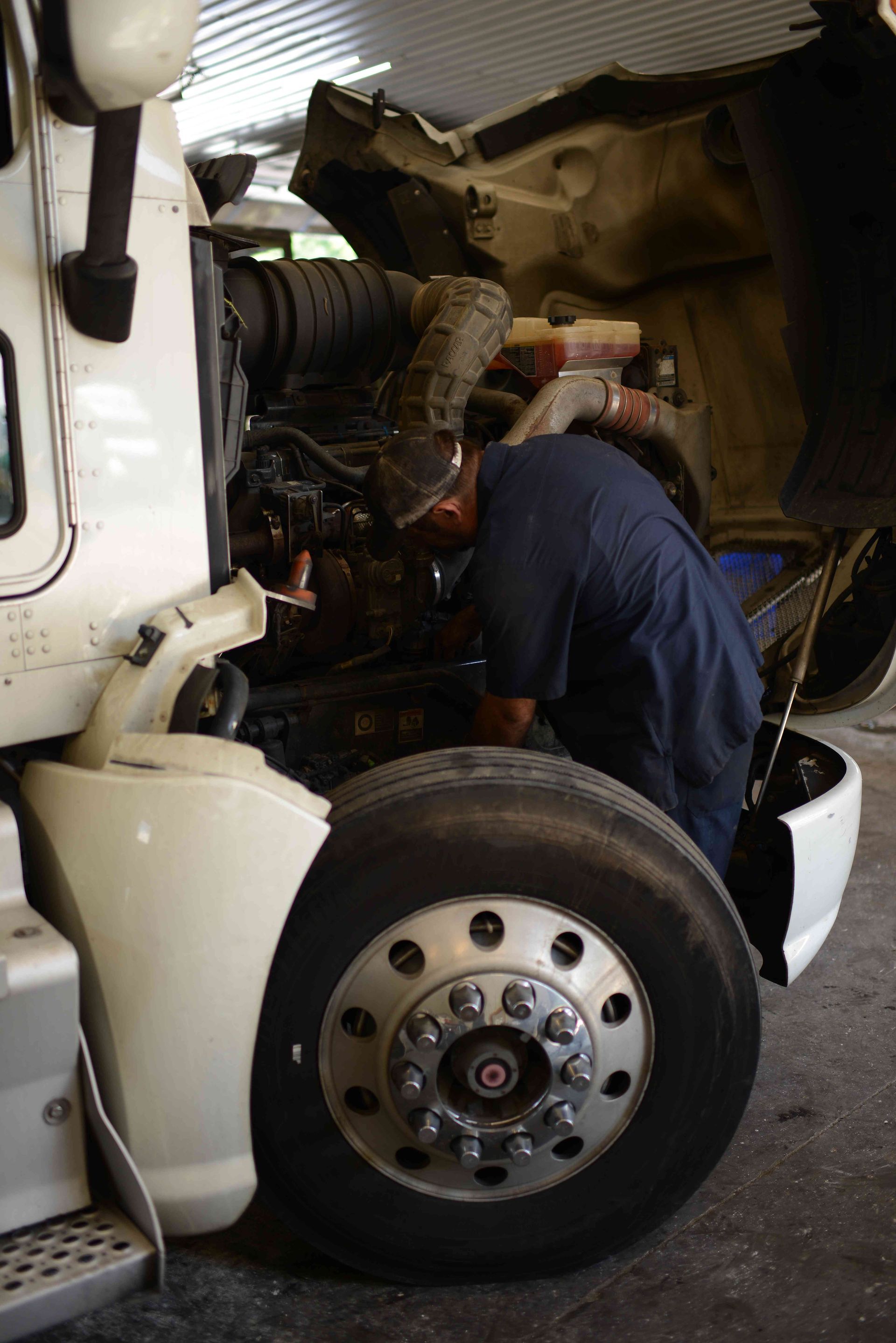 Mechanic working inside a white truck with the hood open and front wheel visible.