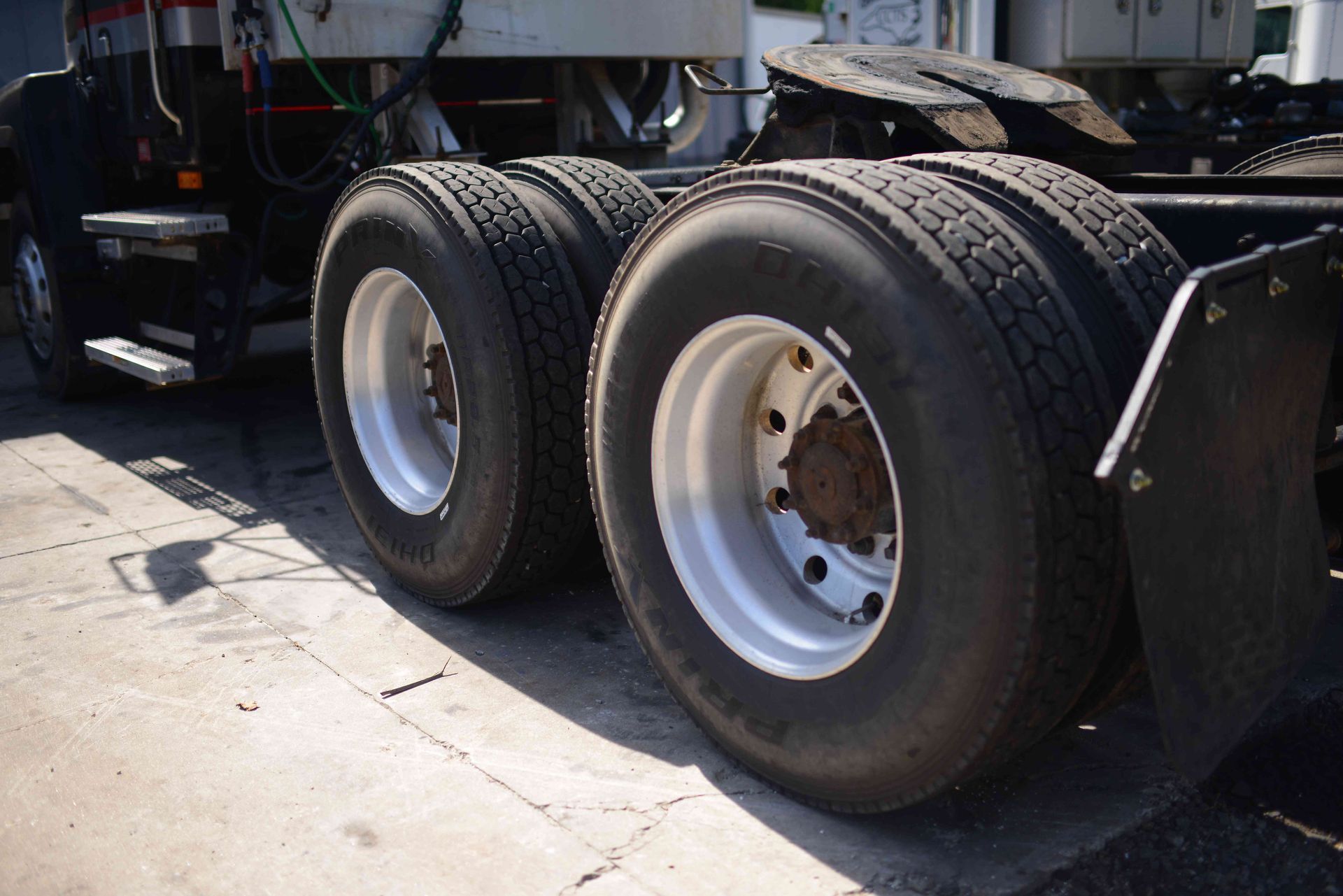 Two large truck tires and wheels on a trailer, parked on pavement in daylight