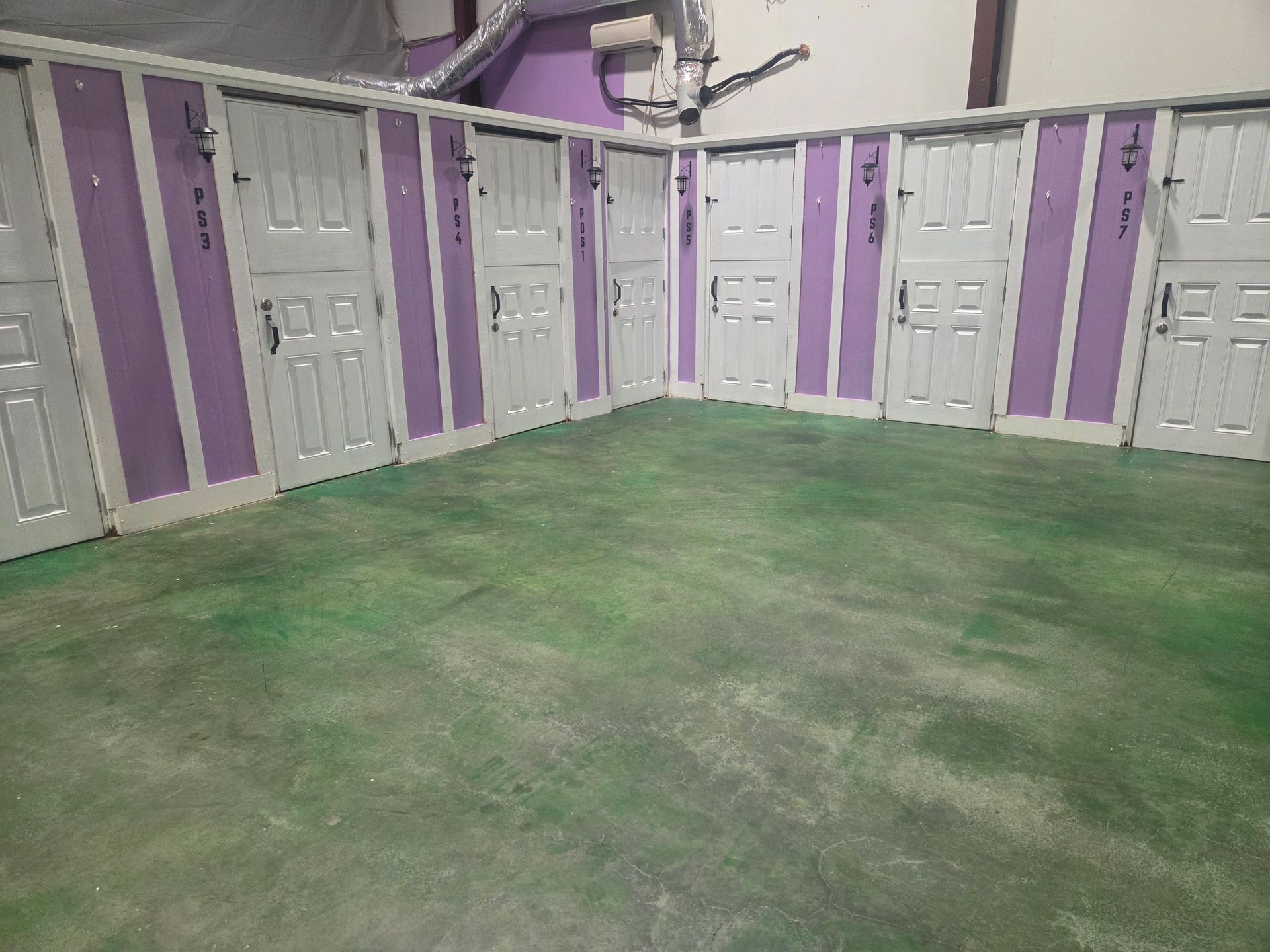 Empty locker room with gray lockers, purple walls, and a green painted floor.