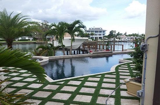 Resort pool with palm trees, stone walkway, and waterfront docks under a cloudy sky