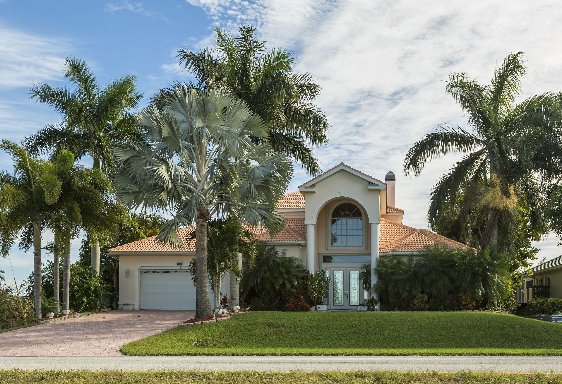 Large two-story stucco house with red tile roof, palm trees, and a green lawn