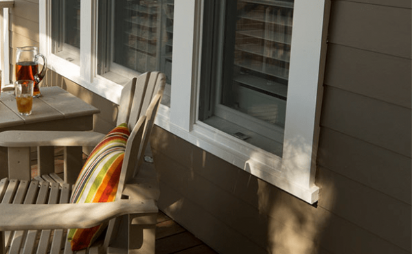 Wooden chair with colorful pillow, next to a table with iced tea, near a window. Exterior shot, sunny day.