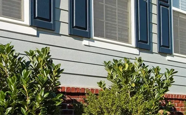 House exterior with blue shutters, light blue siding, red brick, and green bushes.