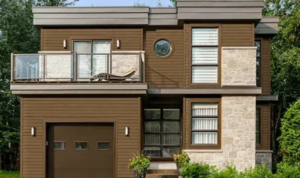Two-story brown house with a garage, balcony, and stone accents, surrounded by trees.