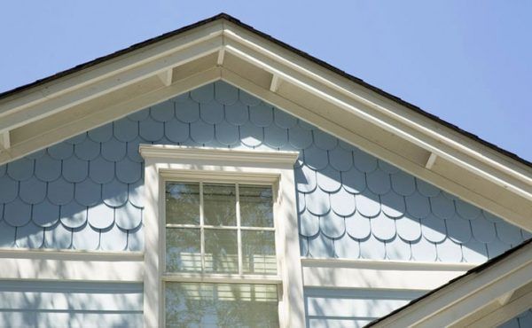 Blue house gable with a window, adorned with white trim and blue shingle siding, against a blue sky.