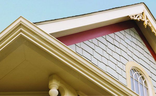 Close-up of a house exterior with decorative trim, light blue shingles, and a window under a light blue sky.