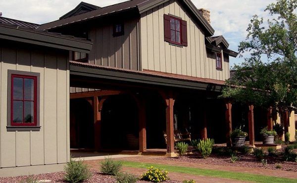 Two-story house with brown siding, red window frames, and a covered porch with wooden columns.