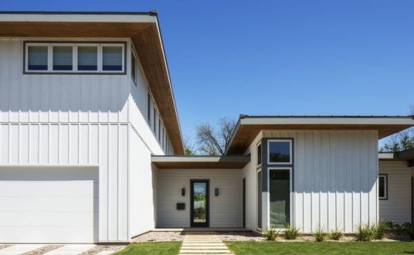 Modern white house with horizontal wood accents, a black front door, and blue sky.