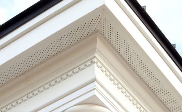 Corner of a building with white decorative trim, small holes for ventilation.