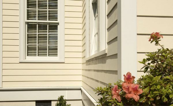Cream-colored house corner with a window, shutters, and pink flowers in front.