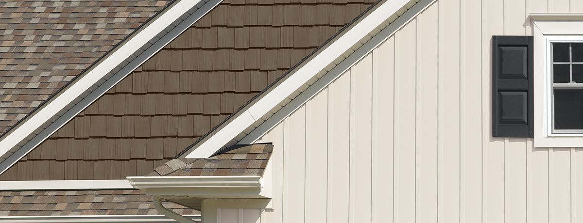 Exterior view of a building with brown shingles, white trim, and a white wall with a black shutter and window.