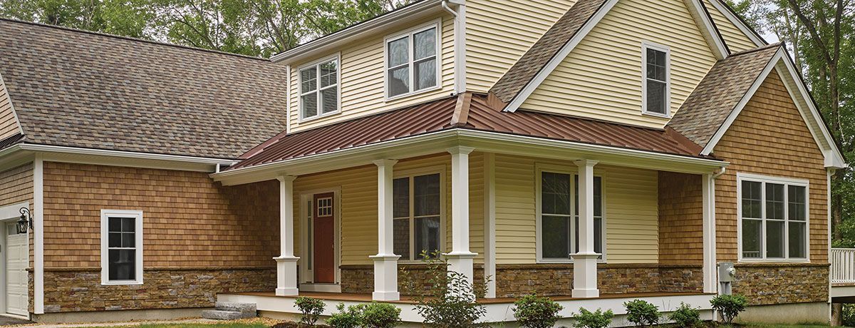 A two-story house with a porch and a brown roof. The house has beige and brown siding.