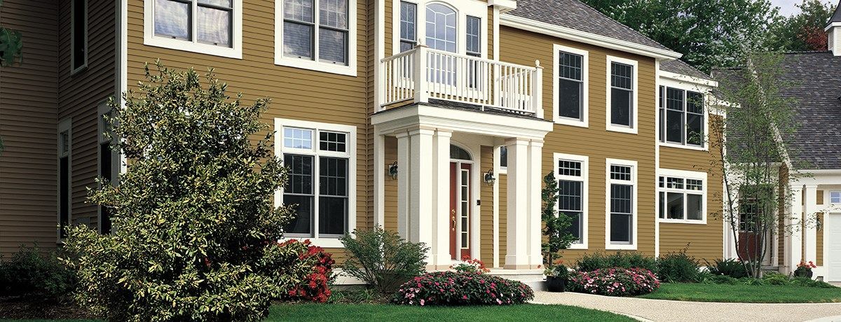 Two-story yellow house with white trim, a balcony, and red door, in front of a green lawn.