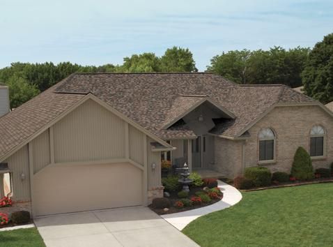 Tan brick house with a brown roof, manicured lawn, and a water fountain near the entrance.