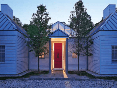 White house with red door between two identical wings, with trees and gravel.